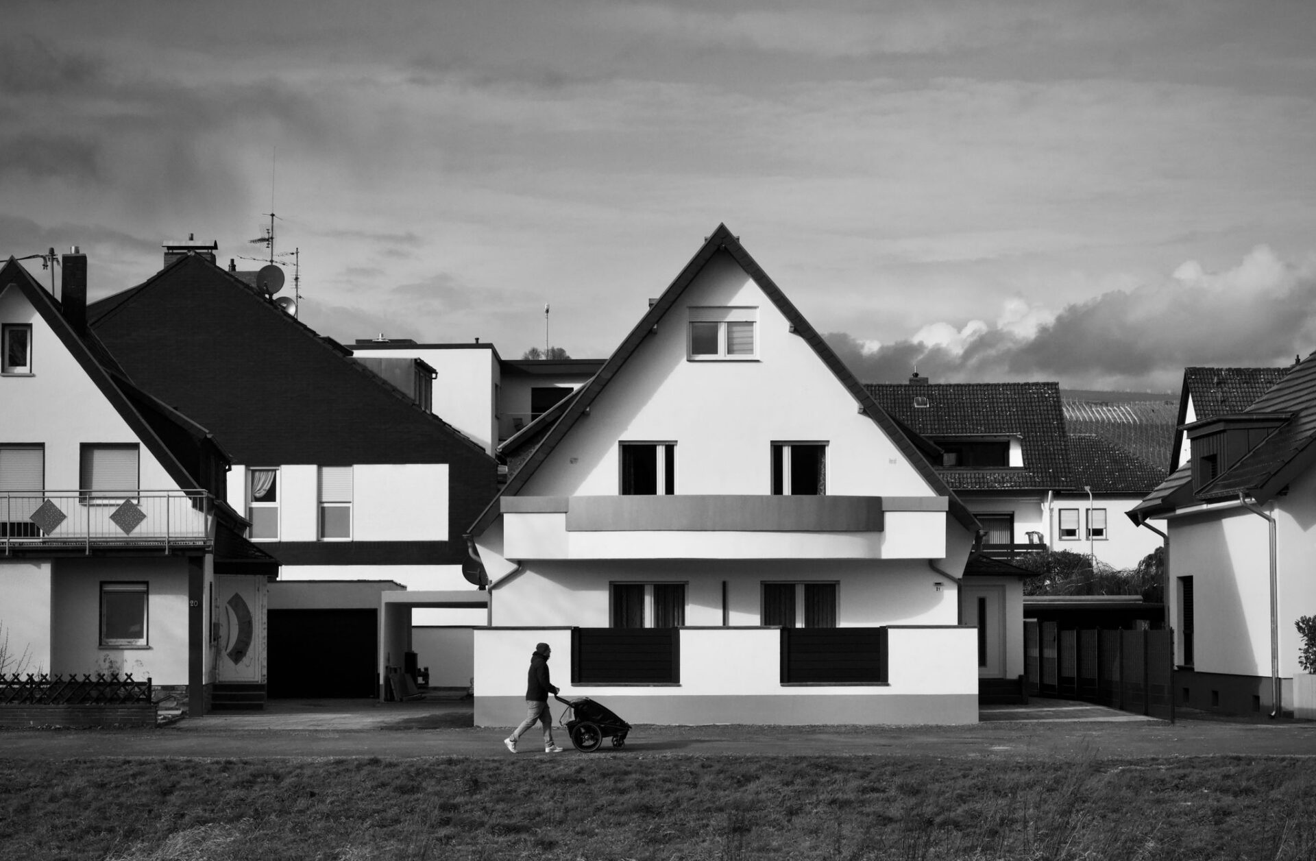 A monochrome view of suburban houses with a pedestrian and stroller on a quiet street.