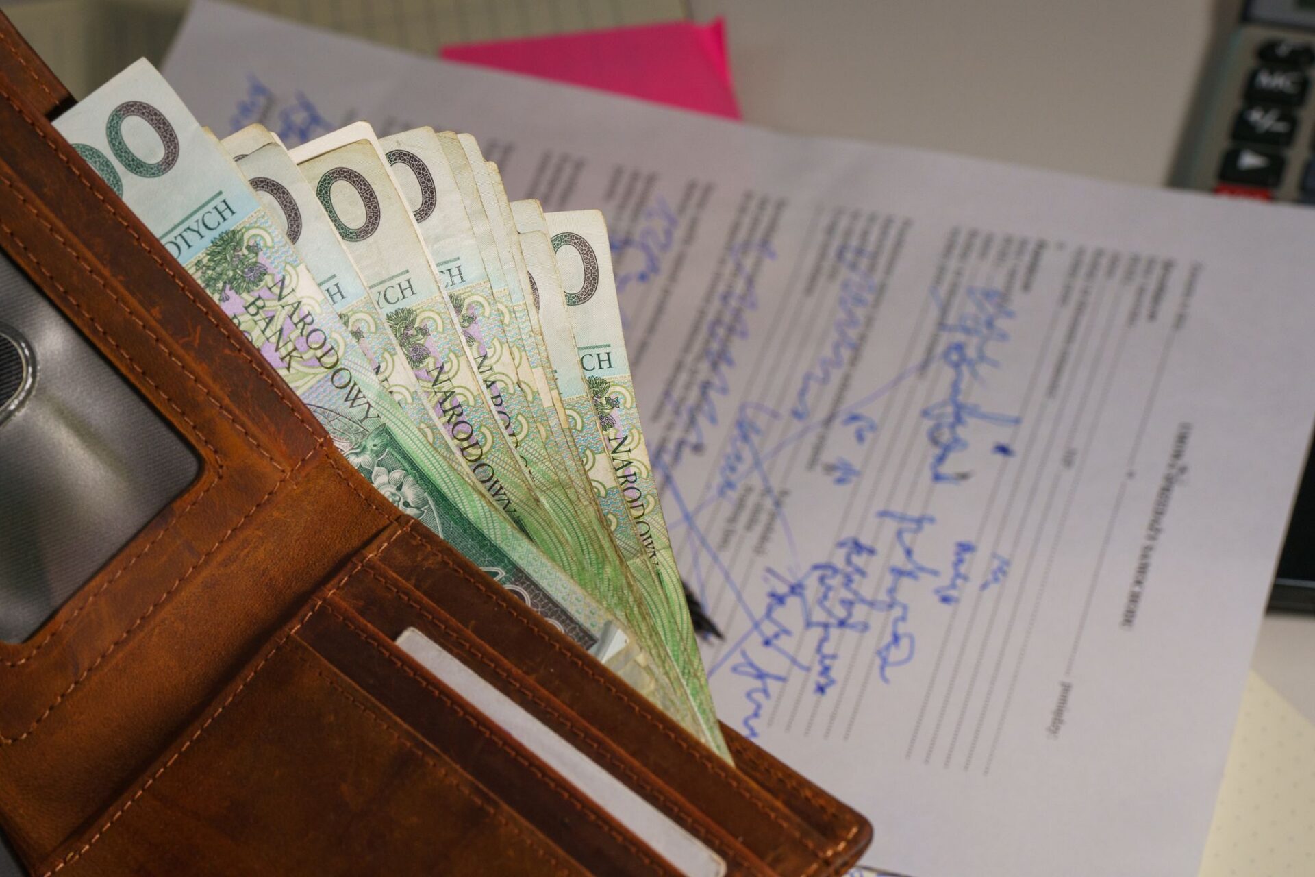 Close-up of a wallet containing Polish Zloty with a signed document in the background, representing financial transactions.